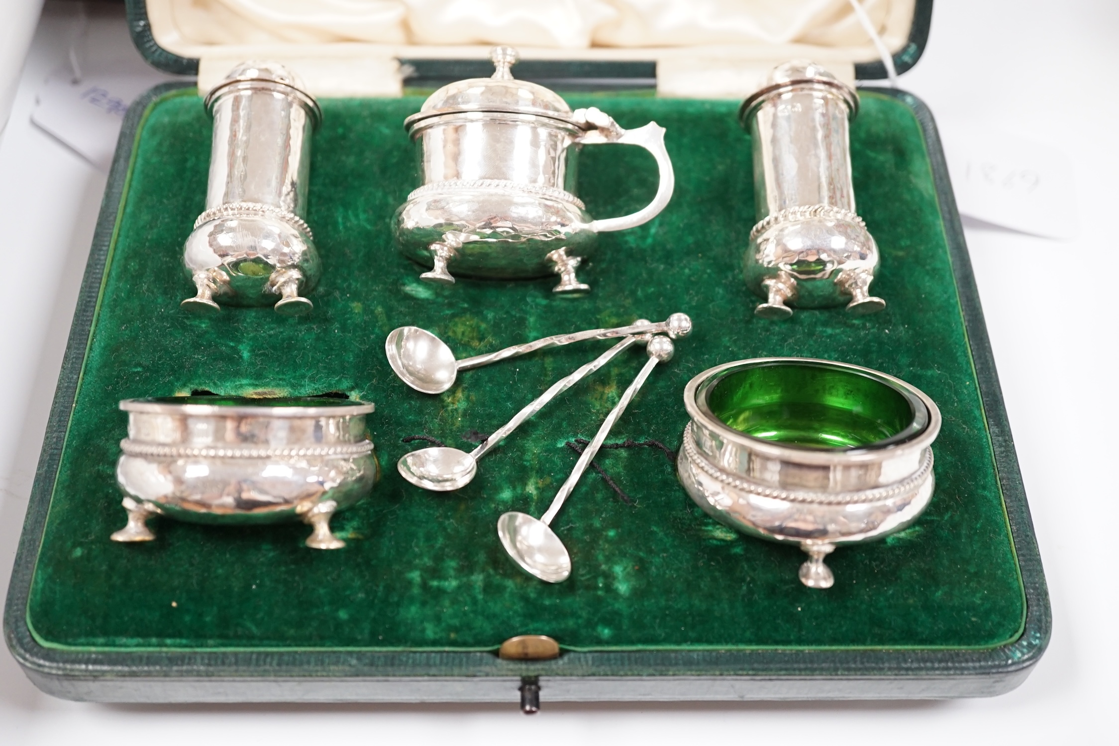 A cased George V planished silver five piece condiment set and three matching spoons by A.E. Jones, Birmingham, 1911.